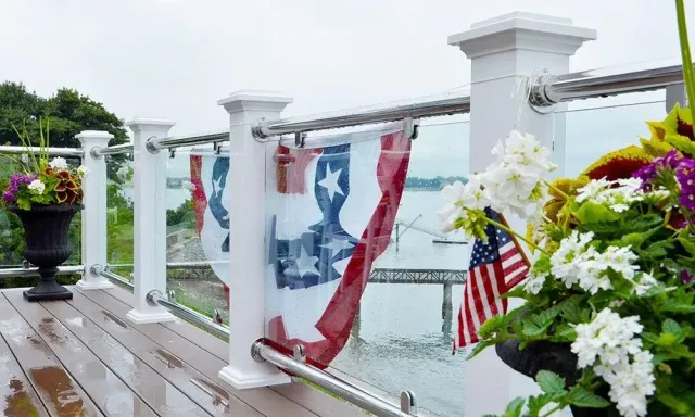 Patriotic bunting and American flags on a white deck railing beside white flowers and a water view