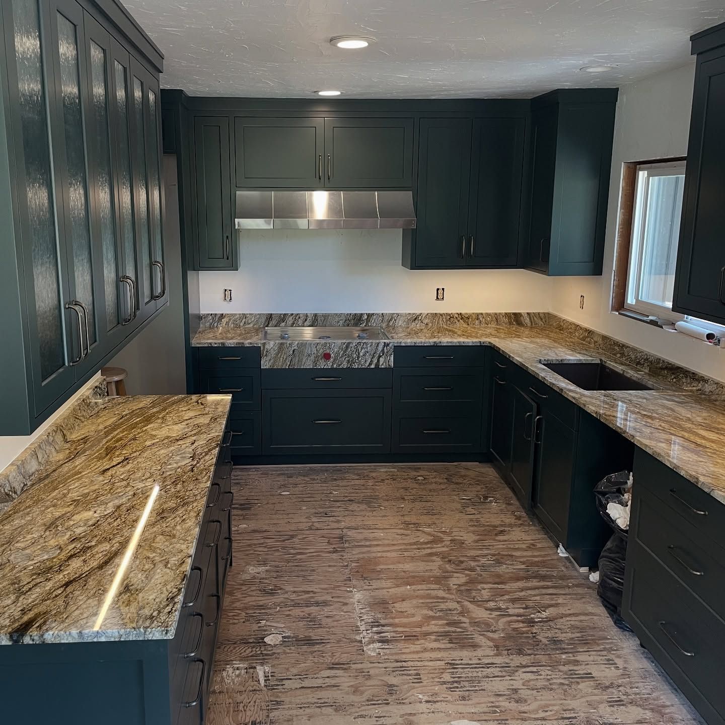 Green kitchen cabinets with granite countertops, in a room with a window and unfinished flooring.