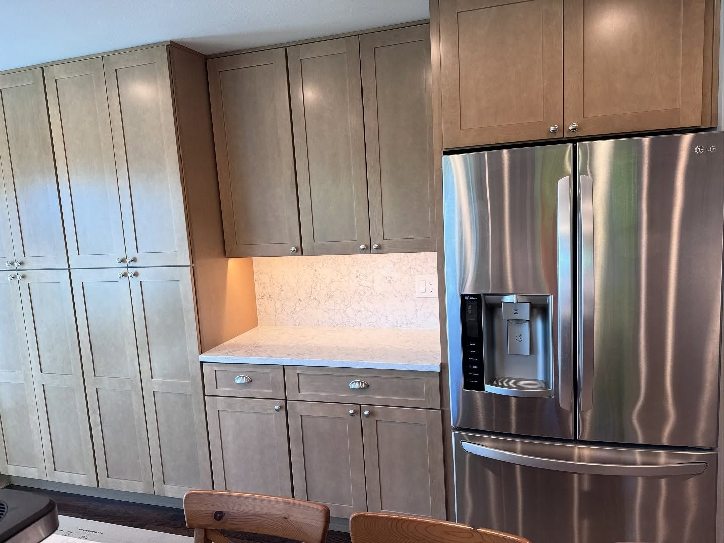 Kitchen with light-colored cabinets, white countertop, stainless steel refrigerator.