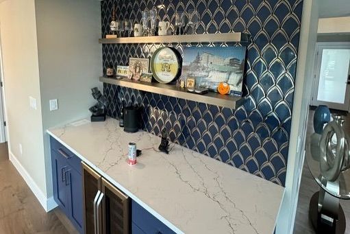 Bar area with blue cabinets, white countertop, patterned blue and gold backsplash, and stainless steel shelves.