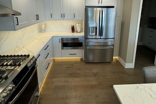 Modern kitchen with white cabinets, stainless steel appliances, and wood flooring.