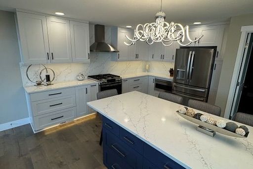 Modern kitchen with white cabinets, blue island, quartz countertops, and stainless steel appliances.