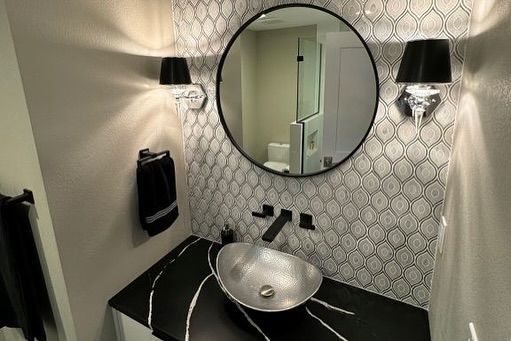 Modern bathroom with black and silver accents: round mirror, patterned backsplash, vessel sink, sconces.