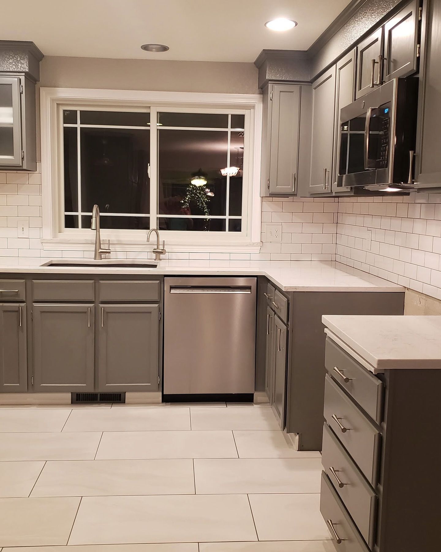 Gray kitchen with stainless steel appliances, white subway tile backsplash, and light-colored countertops and floor.