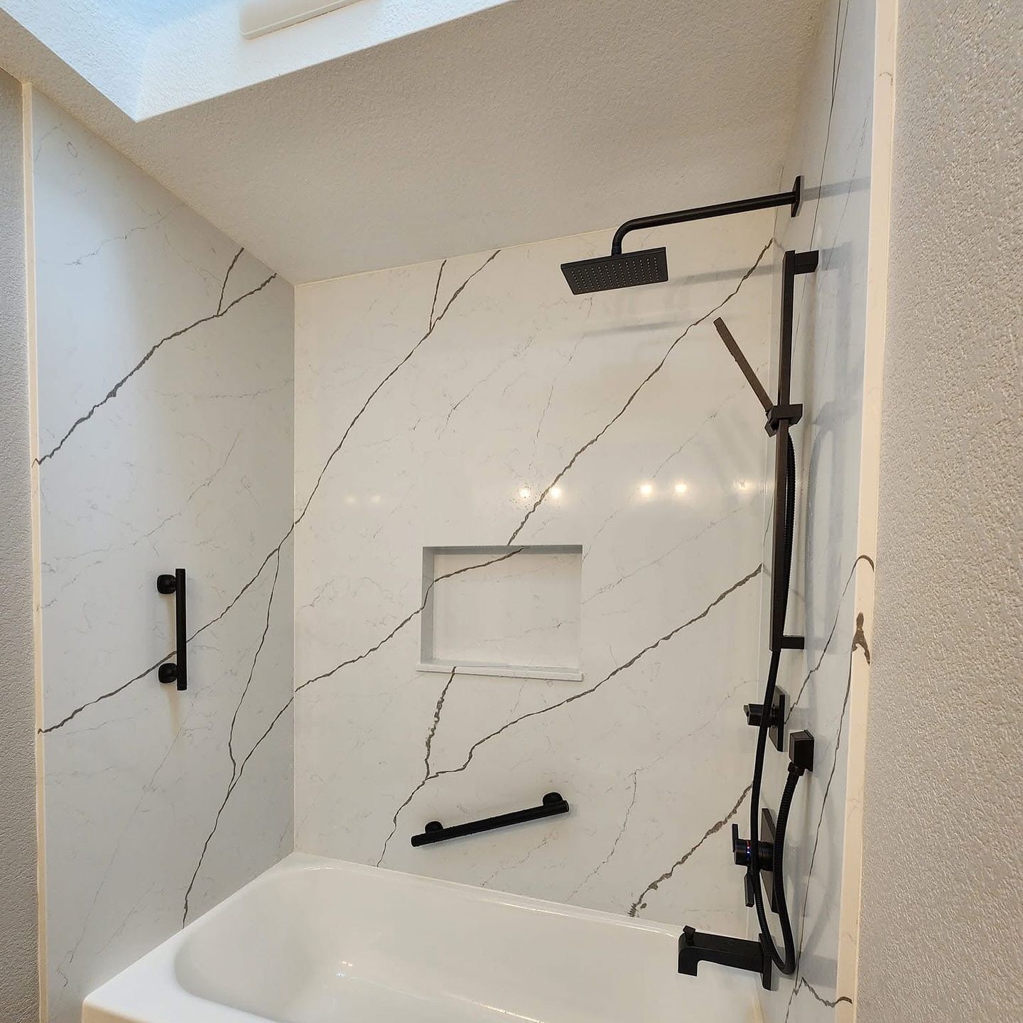Bathroom with white marble-look shower walls and black fixtures, including a shower head, hand bars, and faucet.