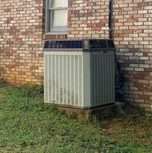 Outdoor HVAC unit beside a brick house wall on a grassy lawn