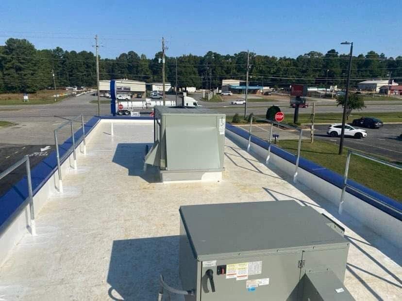 Rooftop with HVAC units and blue railings overlooking a parking lot and trees