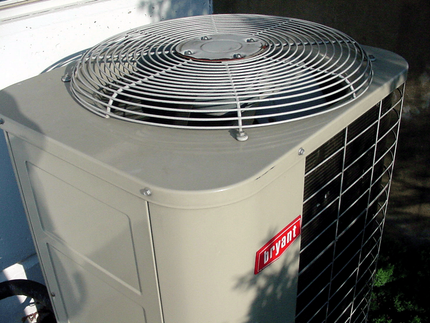 Outdoor air conditioner unit with metal fan grille and red logo on beige housing