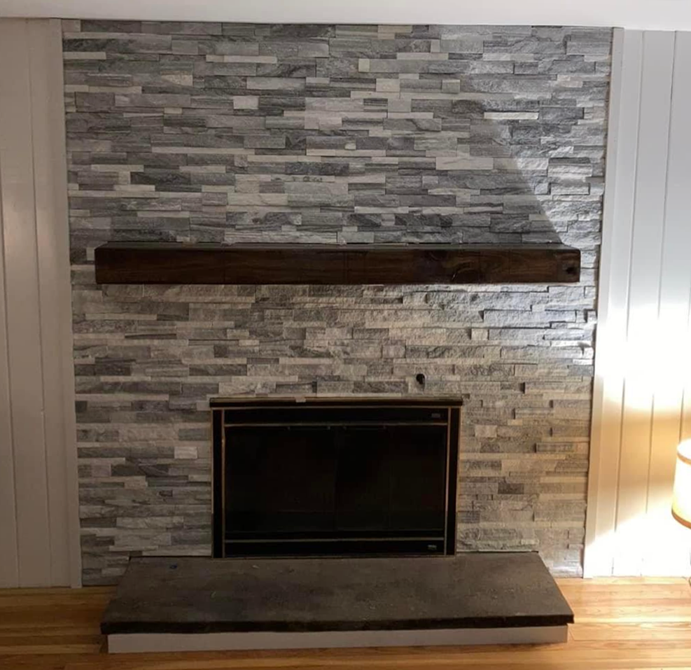 Fireplace with gray stacked stone, a dark wood mantel, and a black fireplace insert.