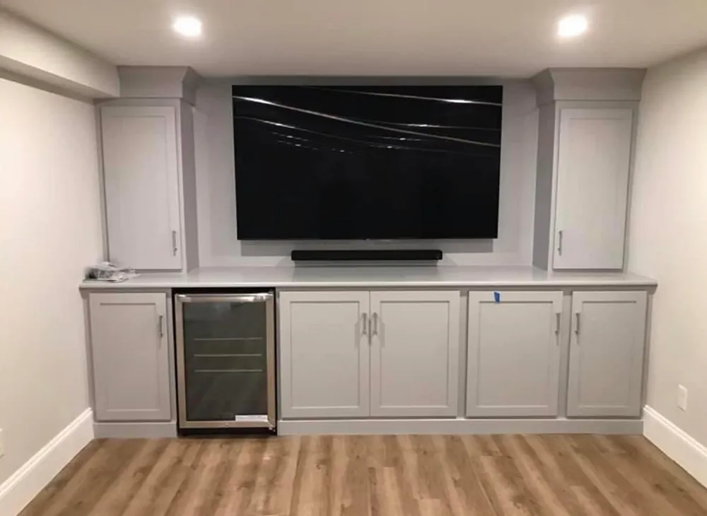 Built-in entertainment center with a large TV, soundbar, and cabinetry; a beverage cooler is on the left.