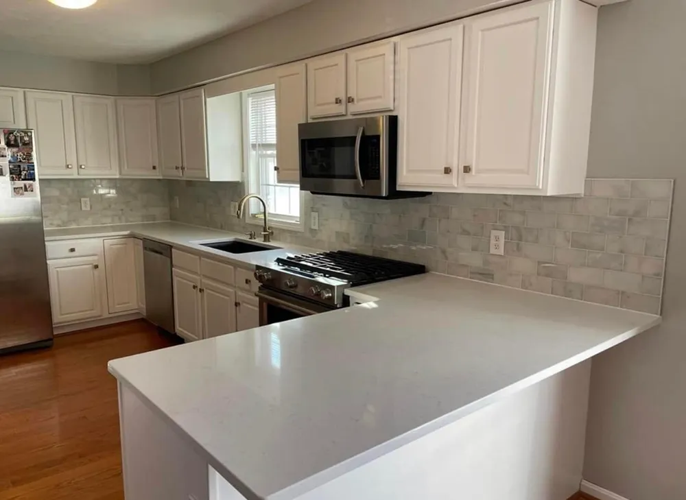 White kitchen with stainless steel appliances, marble backsplash, and white countertop.