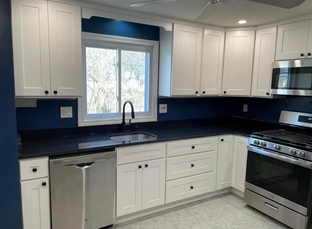 White kitchen cabinets, dark countertops, blue backsplash, stainless steel appliances.