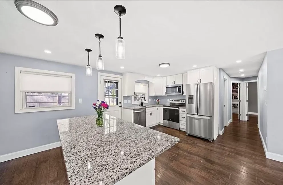 Spacious kitchen with a granite island, white cabinets, and stainless steel appliances.