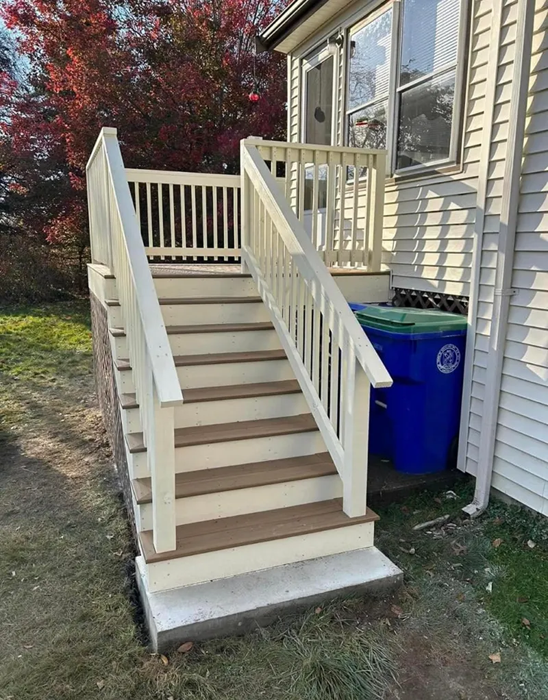 Exterior staircase with white railings, brown steps, and blue trash bin beside the house.
