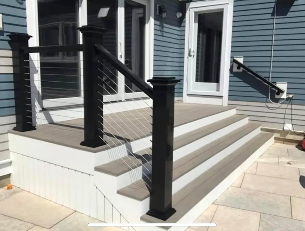 Gray deck steps with black railings and cable infill against blue house.