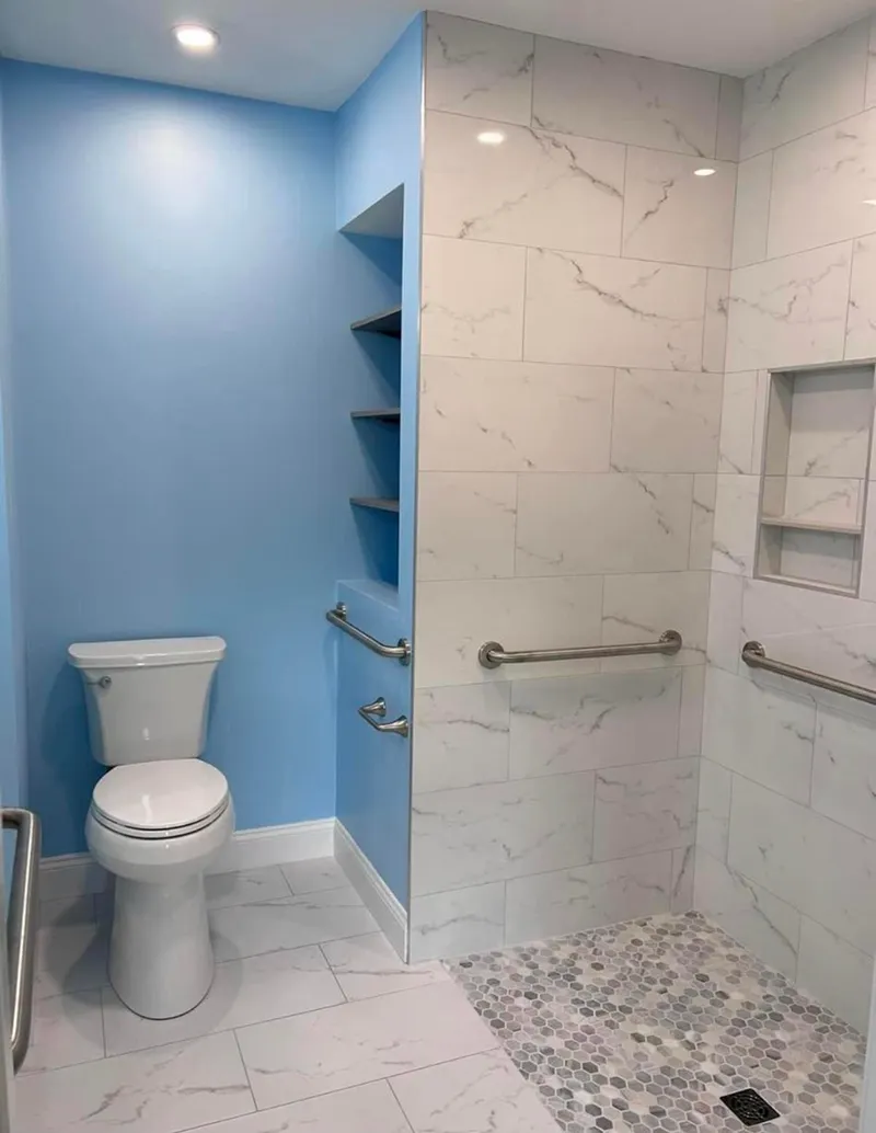 Bathroom with a toilet and shower, featuring grab bars, shelves, and marble-look tiling.