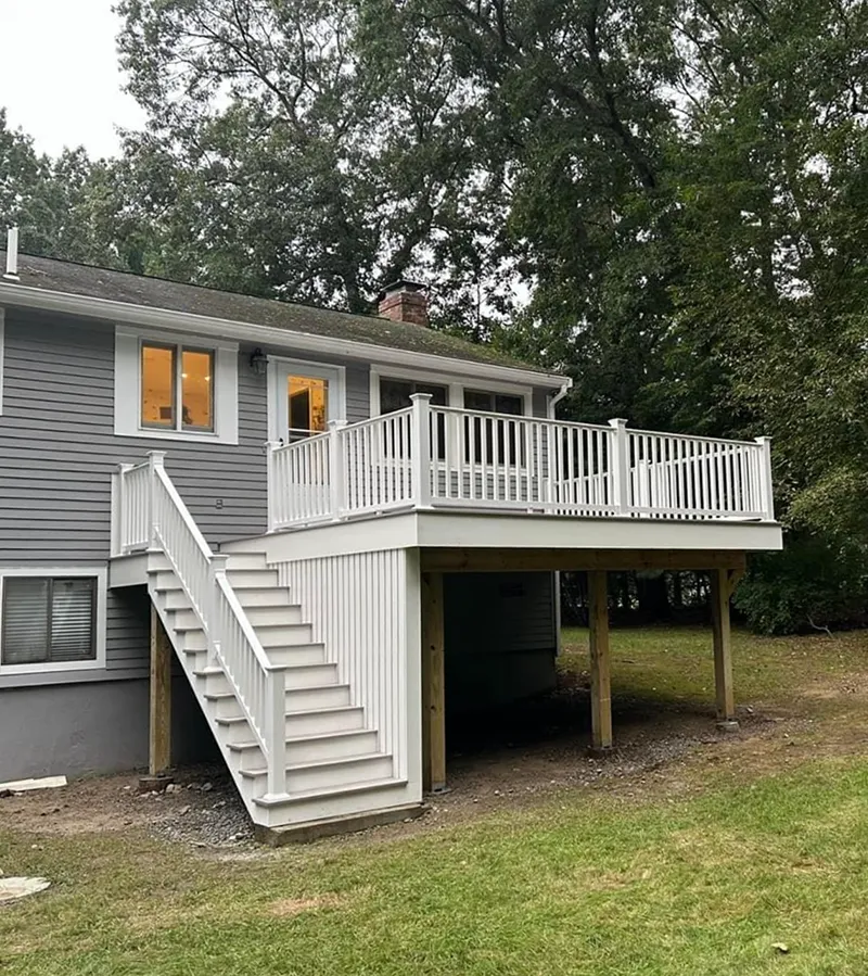 Gray house with a white deck and stairs leading down to a green lawn.