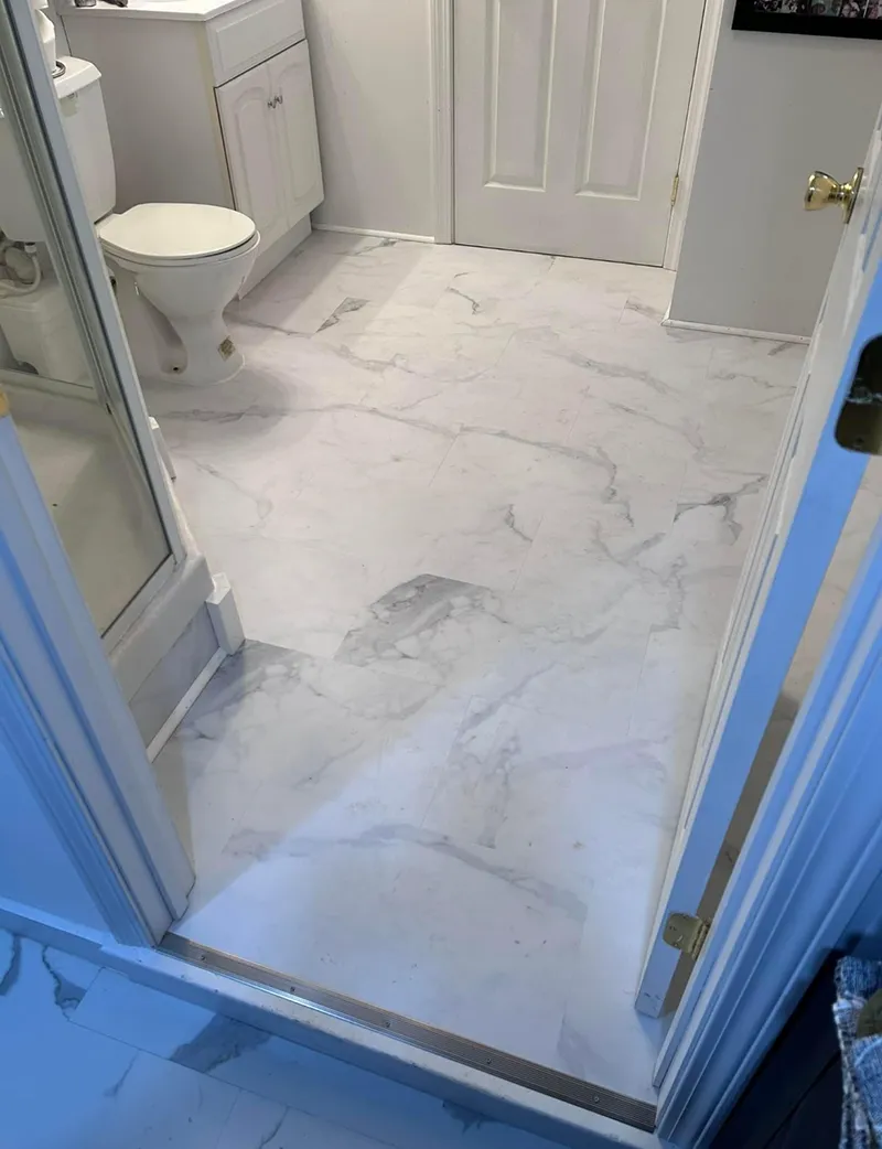 White marble-look bathroom floor with toilet, vanity, and closed door.
