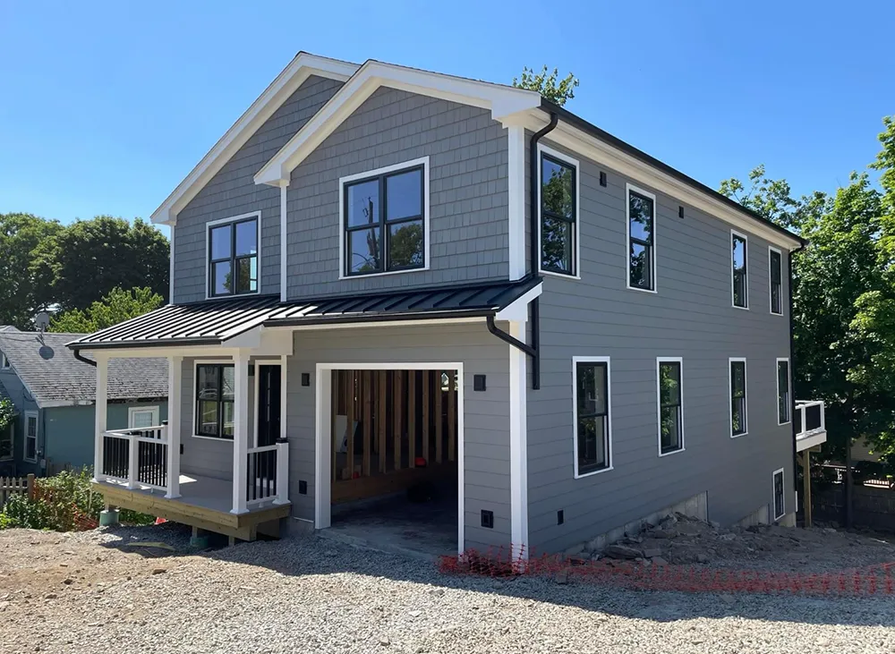 Gray two-story house with black trim, open garage, and a porch under a clear sky.