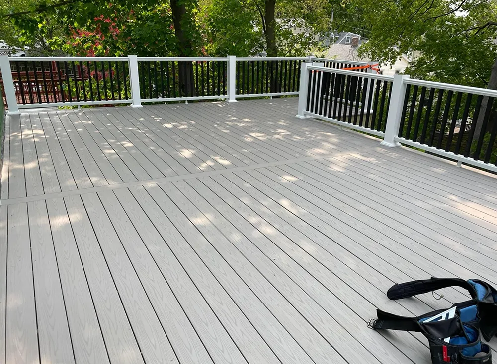 Wooden deck with white railing posts, black balusters, and gray decking, surrounded by trees.