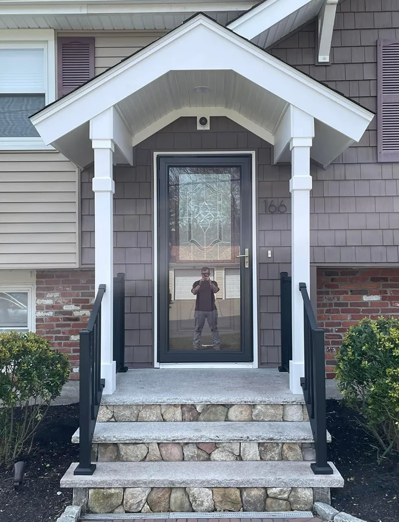 A house entryway with a porch, steps, and a person reflected in the screen door.