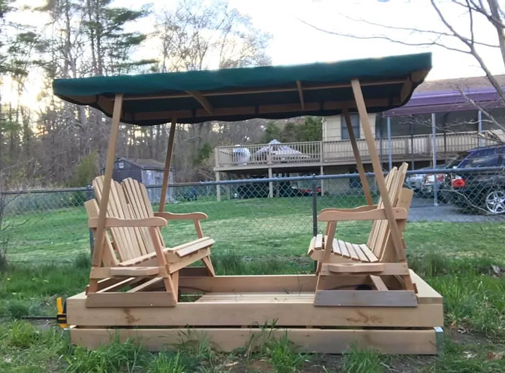 Wooden double swing set with green canopy, in grassy yard.