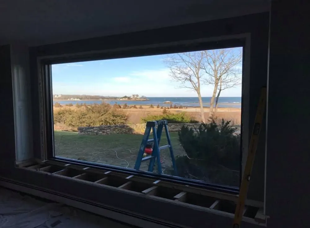 Interior view of a large window overlooking a beach with a ladder and level visible.