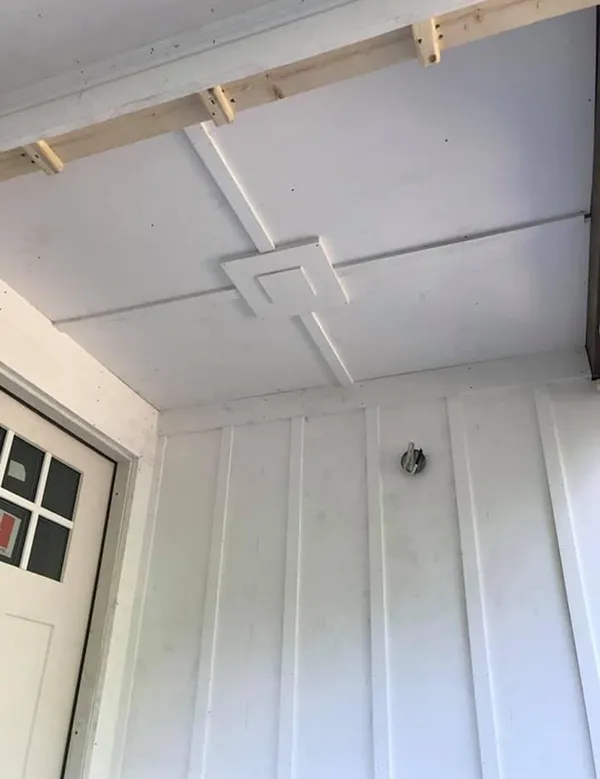 White porch ceiling with decorative trim. Vertical white paneling on the wall, door on the left.