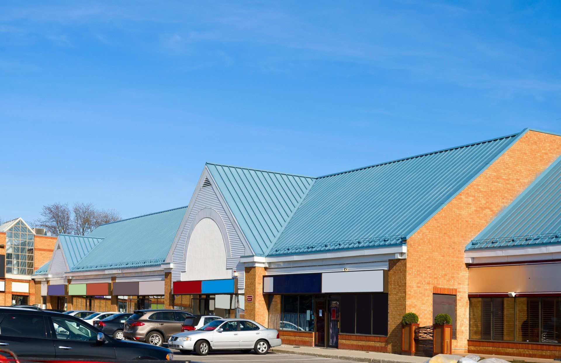 Strip mall with blue roof, brick facade, parked cars, clear sky.