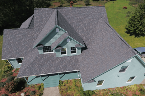 An aerial view of a house with a gray roof and teal siding, set in a grassy yard.