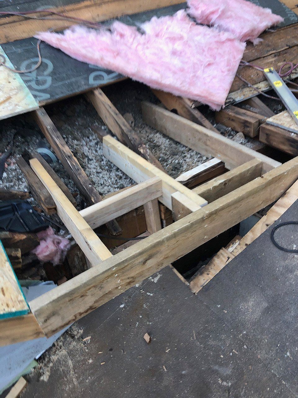 Overhead view of roof repair: exposed wood framing, insulation, and new plywood.