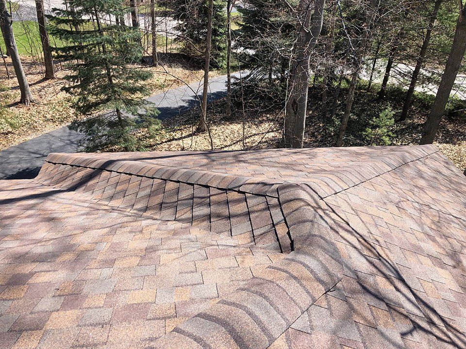 Damaged asphalt shingle roof, with missing and lifted shingles, showing weathering and wear.