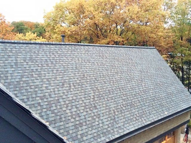Gray shingled roof with a background of fall trees.