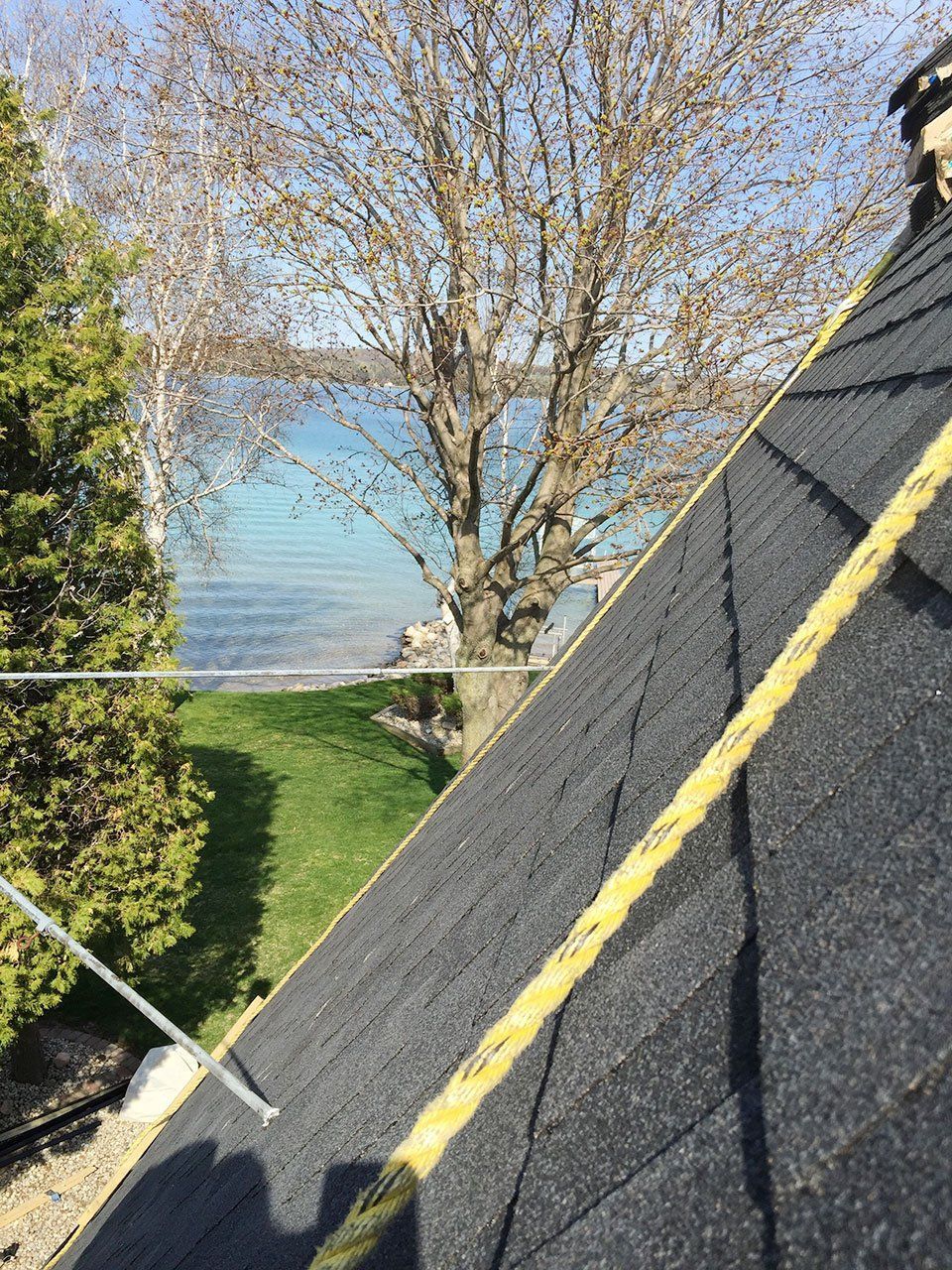 Black shingled roof with a safety rope, overlooking a lake and trees.