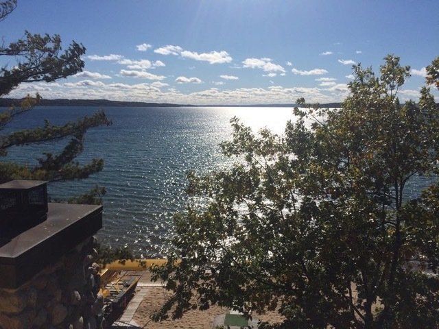 Bright sun reflects on a rippling lake, seen from behind trees and a stone structure on a sunny day.
