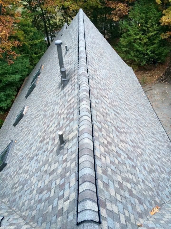 View of a house roof, covered in patterned gray shingles, with a ridge cap and chimneys.
