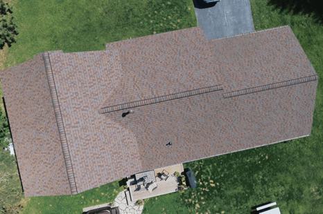 Overhead view of a brown shingled roof with a patio and green lawn.
