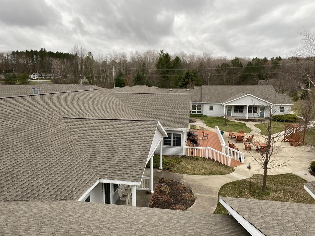 Roofs of several white buildings, deck and patio, cloudy sky, trees in the background.