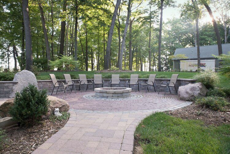 A patio with a fire pit and chairs in the middle of the woods.