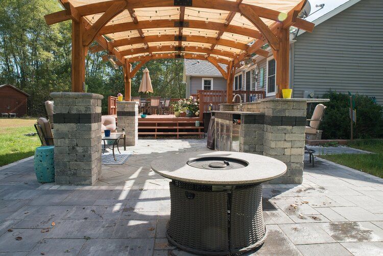 There is a fire pit in the middle of the patio under a pergola.