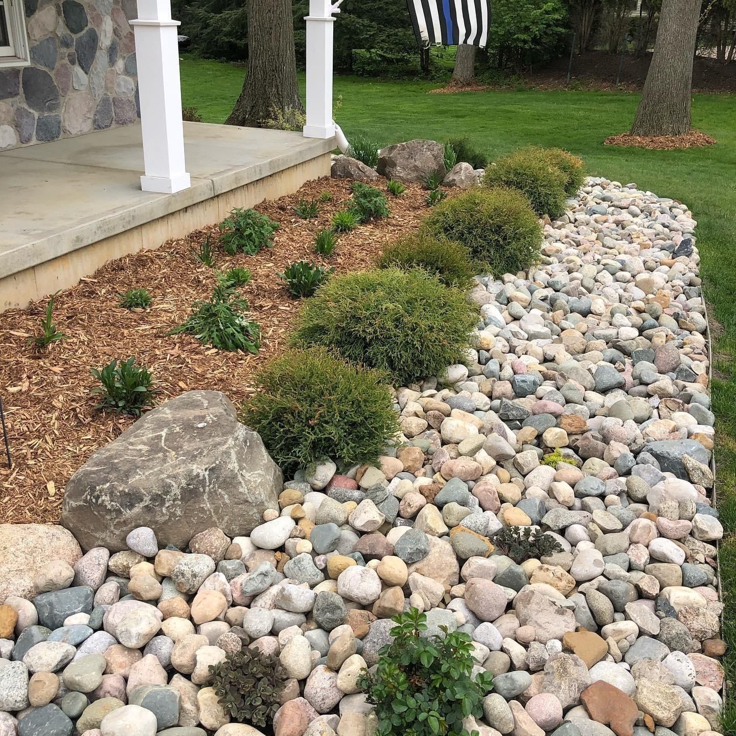 a rock garden in front of a house with a flag in the background