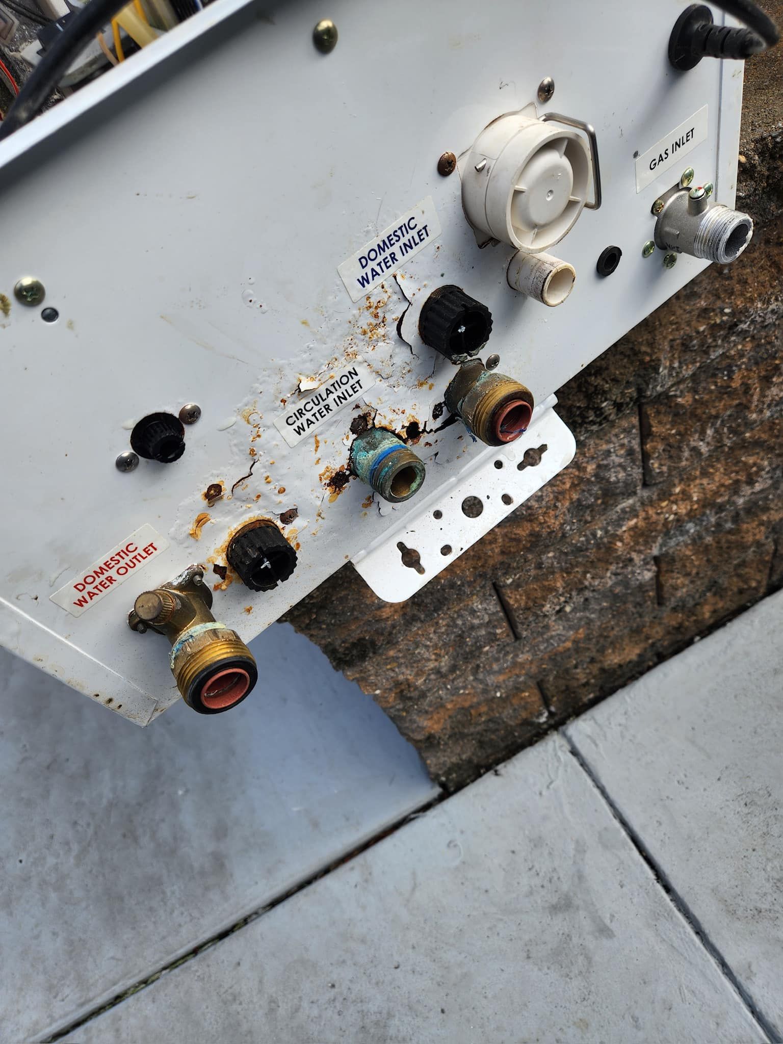 A white item with a lot of brass fittings on it is sitting on a sidewalk.