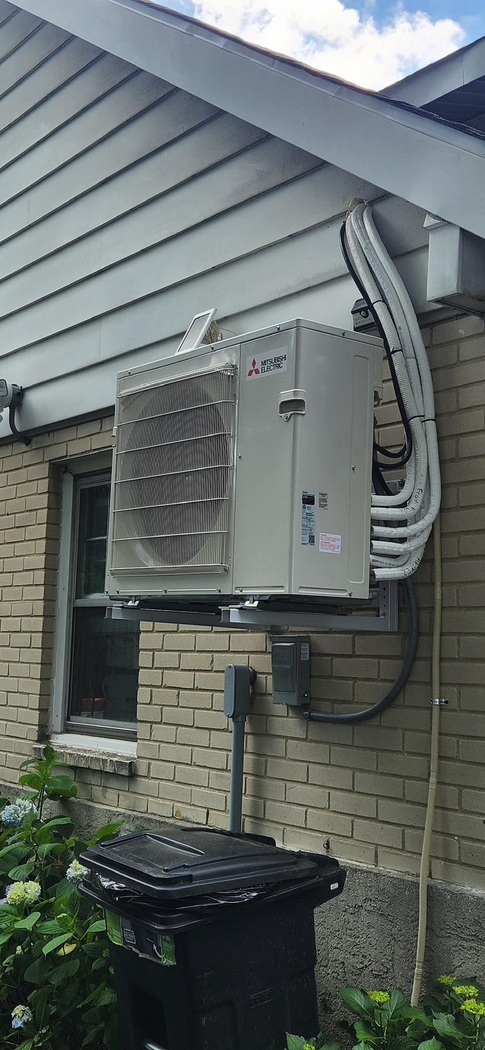 A large air conditioner is mounted on the side of a brick house.