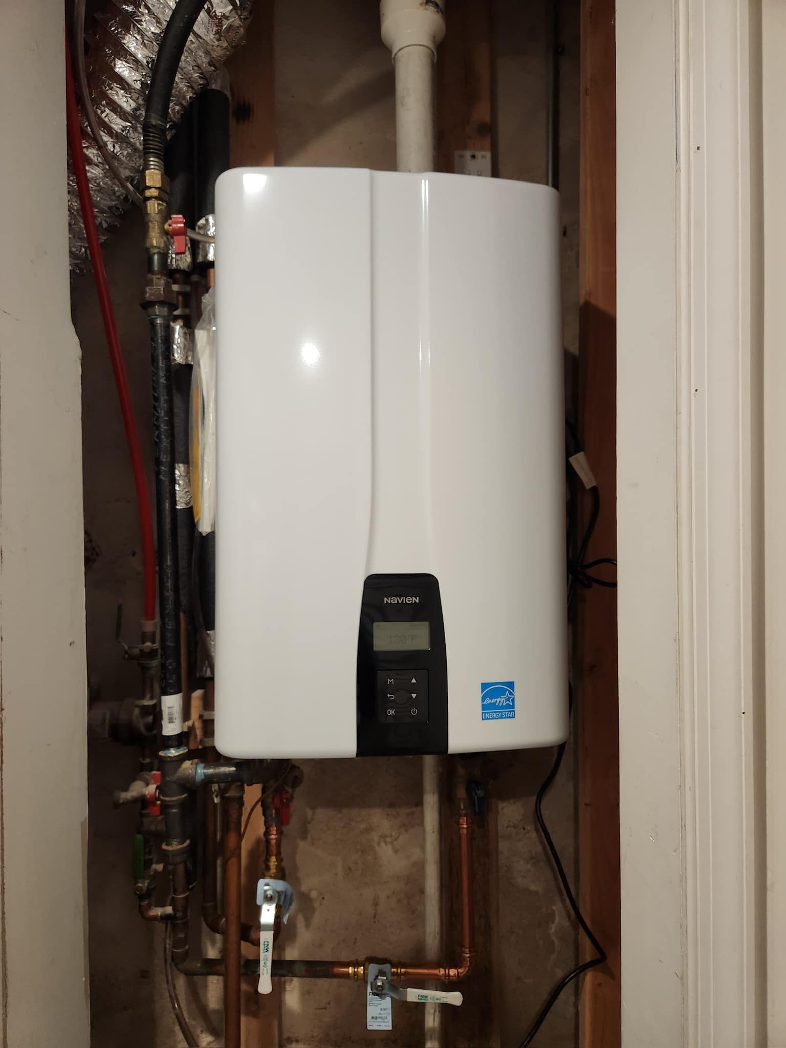 A white water heater is hanging on a wall next to copper pipes.