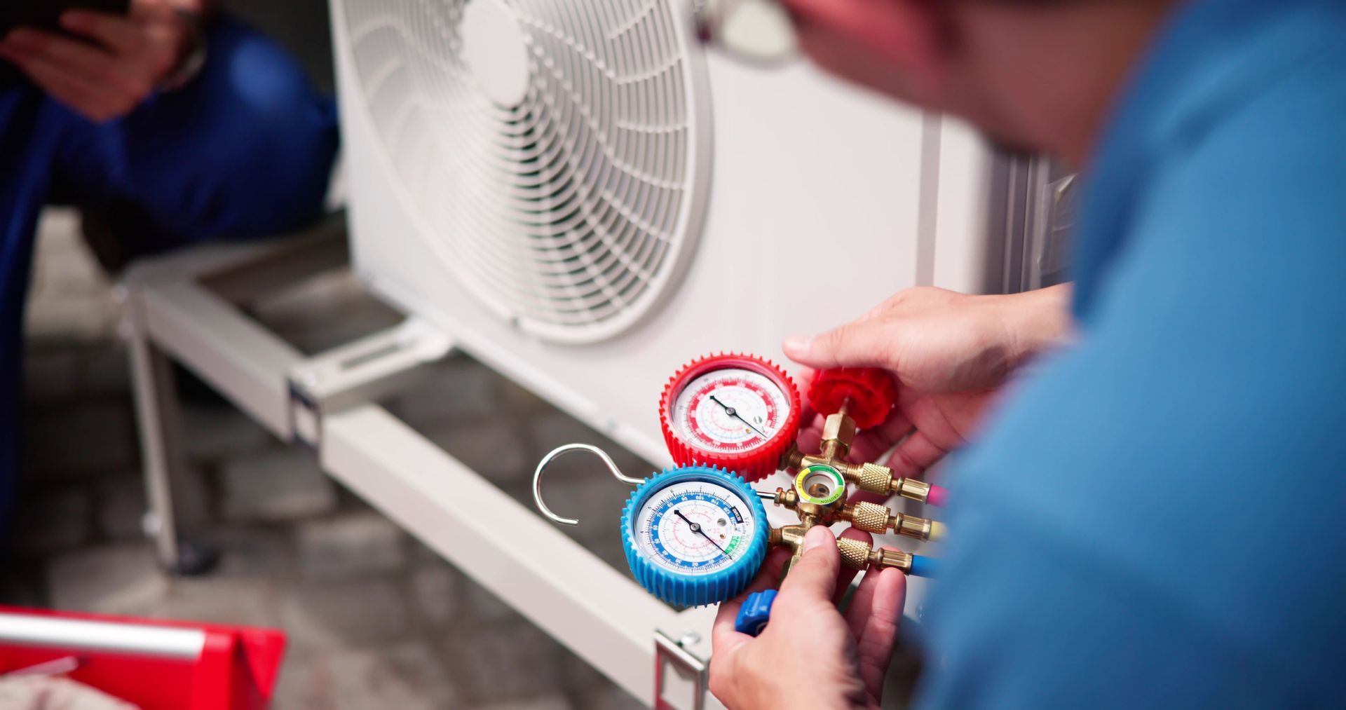 HVAC technician connecting gauges to an air conditioning unit. Close-up on the gauges and hands in a white room.