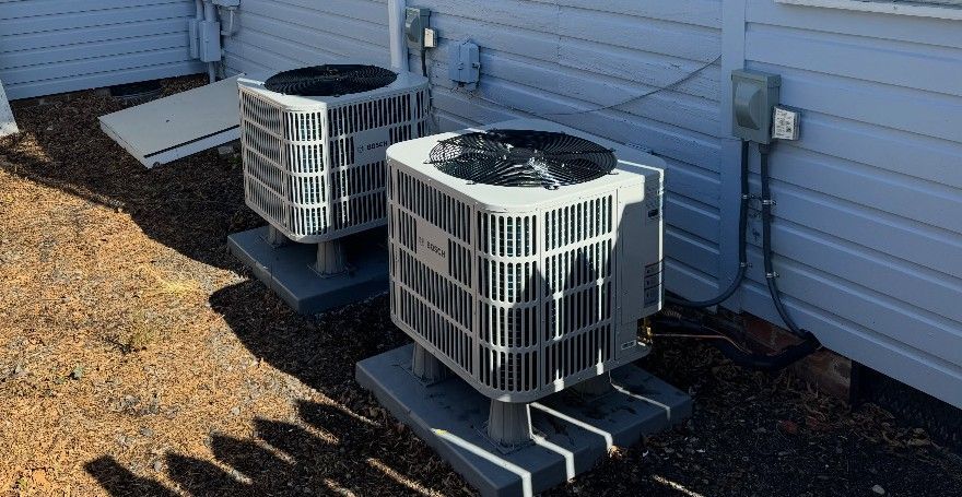 Two outdoor air conditioning units beside a house wall on a gravel bed