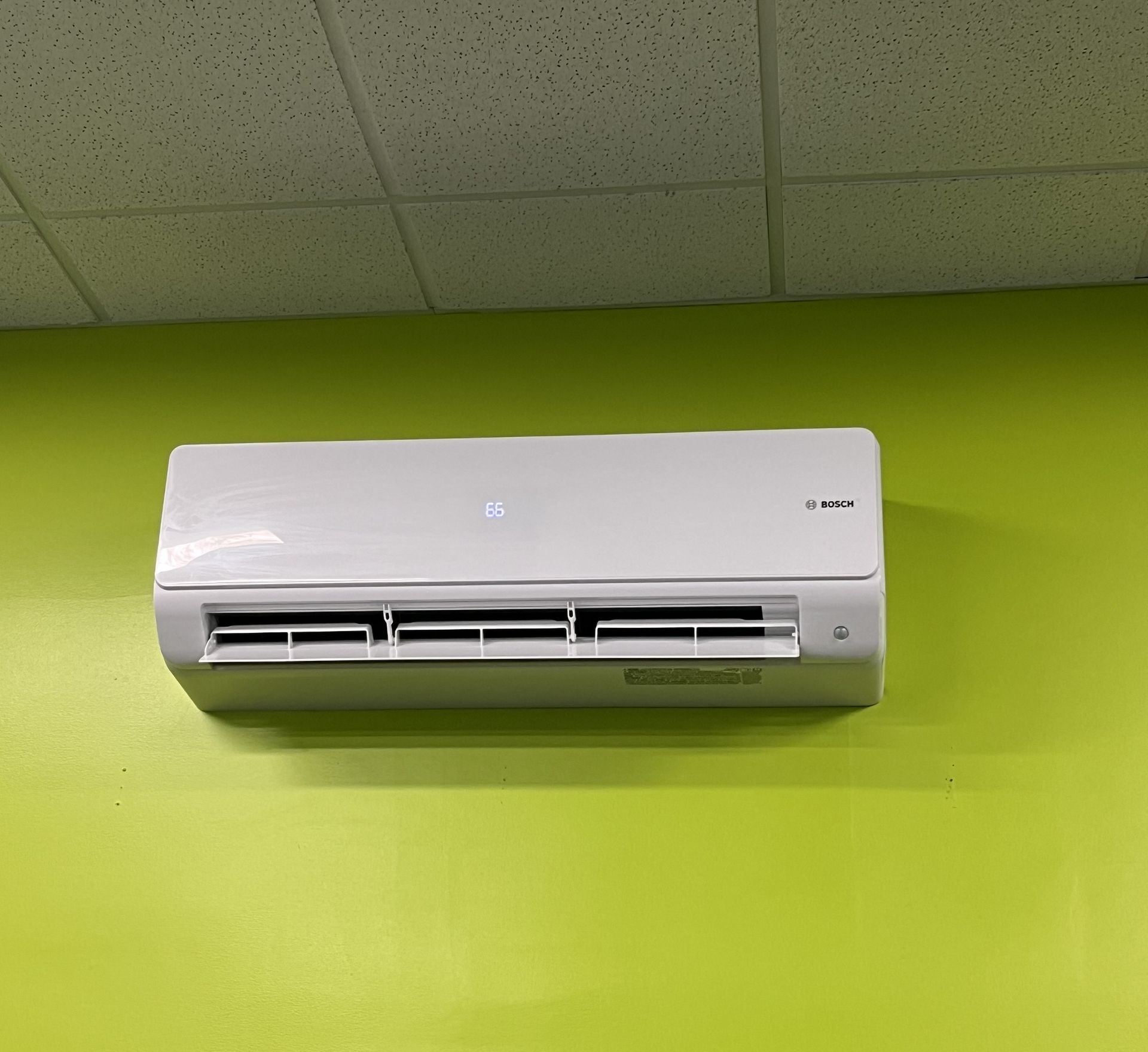 White wall-mounted air conditioner on a bright green wall near the ceiling