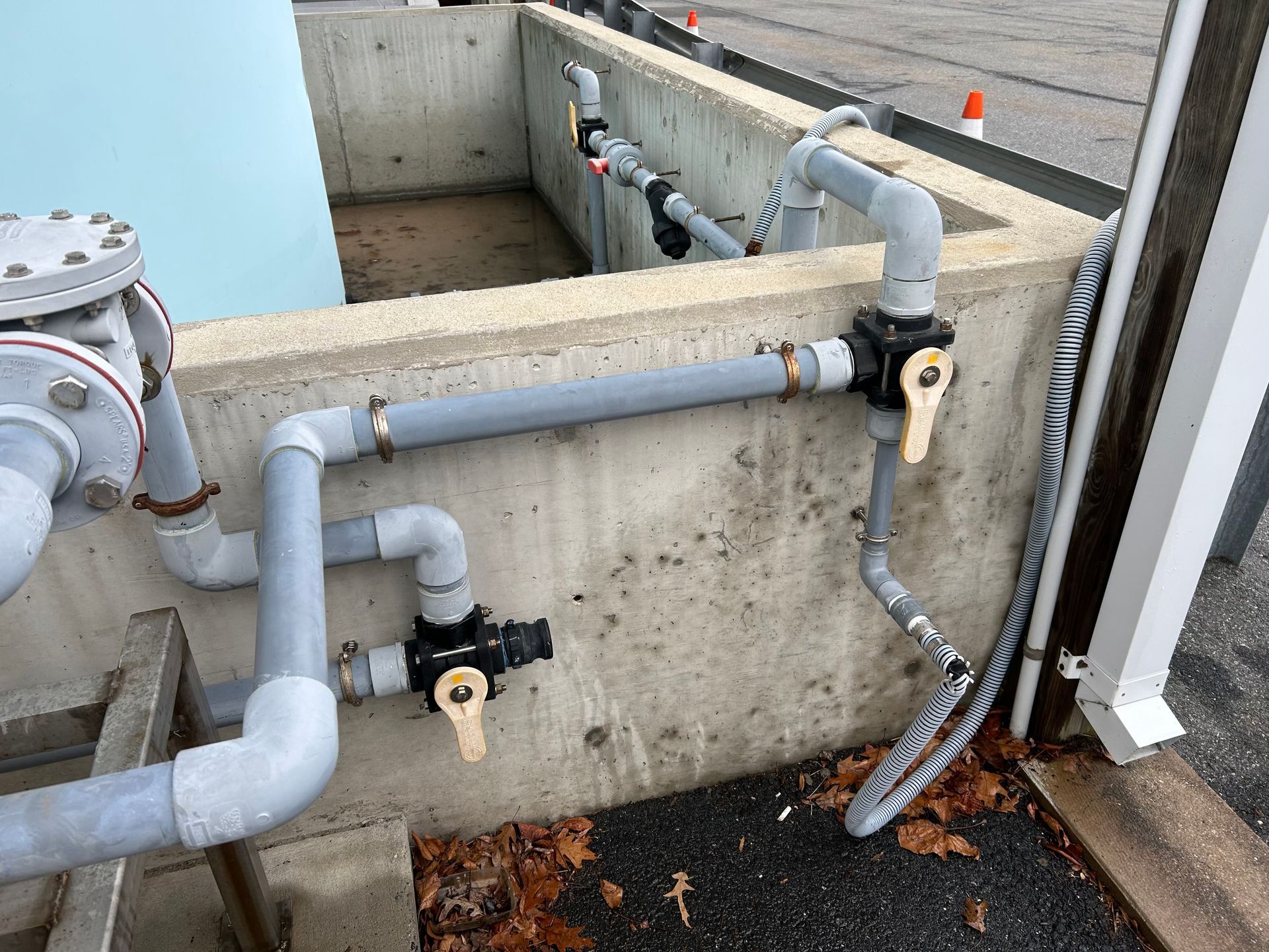 Concrete utility pit with gray pipes and black valves beside a building wall