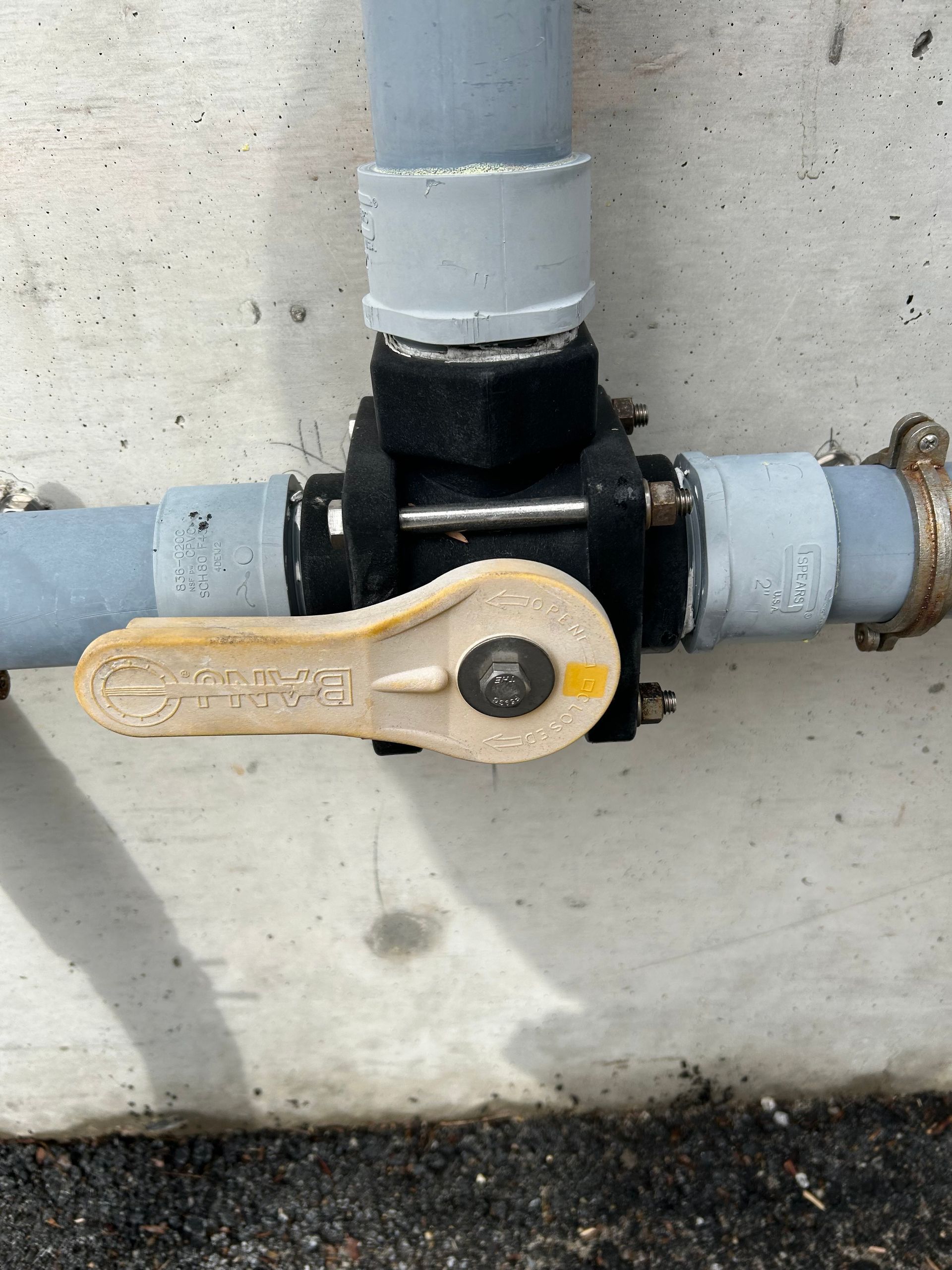Yellow valve handle on a black water pipe against a concrete wall