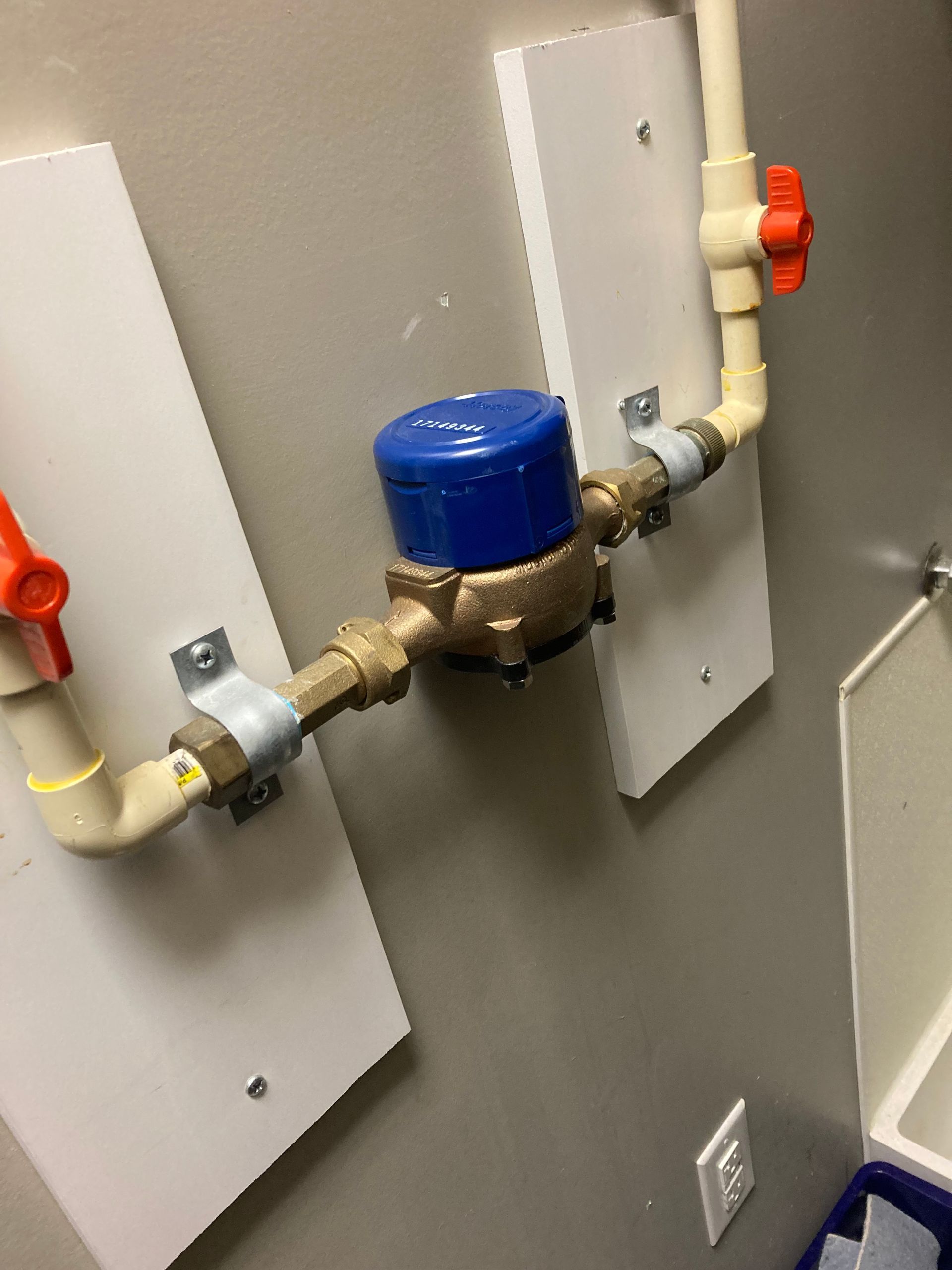 Water meter with blue cap and red shutoff valves mounted on a gray utility wall